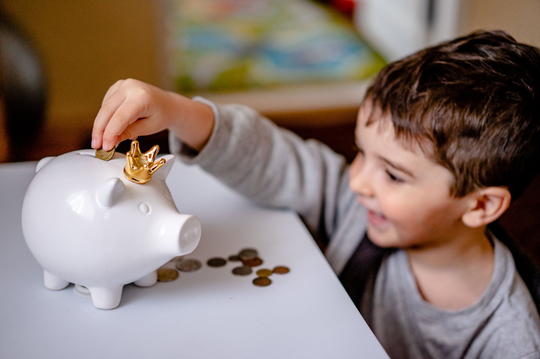 boy in gray long sleeve shirt putting coins in a piggy bank